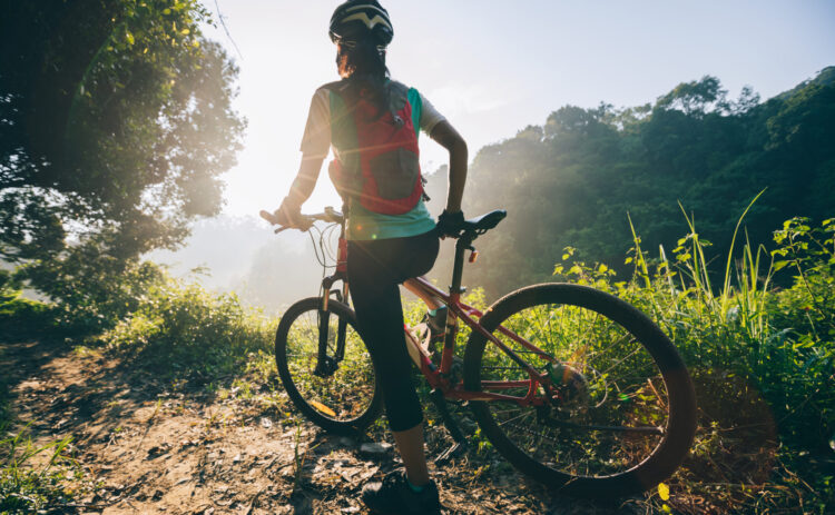 Young woman cyclist carrying mountain bike on summer forest trail