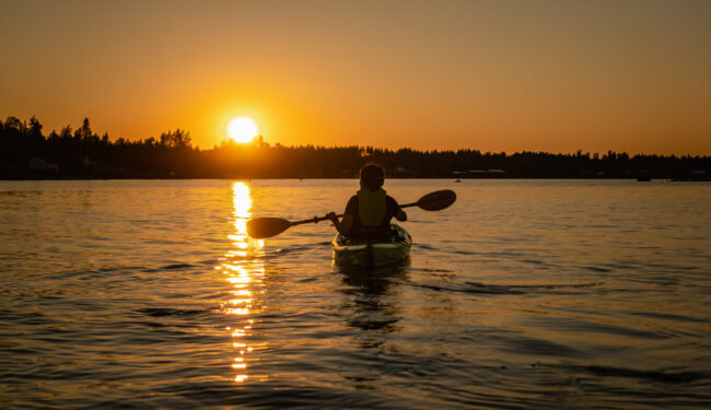 Girl kayaking and taking pause calm sea at midnight in Northern Sweden during light Summer nights. All day around Sun in polar regions.